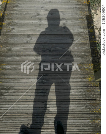 Shadow of a pilgrim with backpack on wooden boardwalk along the Camino de Santiago route, sunny day, minimalistic travel scene 136309004