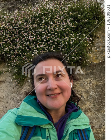 Smiling solo female pilgrim taking selfie near stone wall covered with small white wildflowers along Camino de Santiago route Smiling solo female pilgrim taking selfie near stone wall covered with small white wildflowers along Camino de Santiago route 136309031