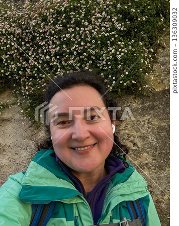 Smiling solo female pilgrim taking selfie near stone wall covered with small white wildflowers along Camino de Santiago route Smiling solo female pilgrim taking selfie near stone wall covered with small white wildflowers along Camino de Santiago route 136309032