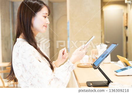 A young woman scanning a QR code to pay at a cafe A young woman scanning a QR code to pay at a cafe 136309218