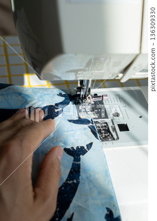 person sews product made blue fabric on sewing machine. tailor focused on work, calm relaxed mood. person sews product made blue fabric on sewing machine. tailor focused on work, calm relaxed mood. 136309330