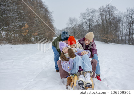 Family enjoying winter sledding together on snowy hill. 136309801