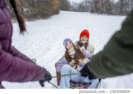 Parents pulling daughters on sled through winter landscape. 136309804