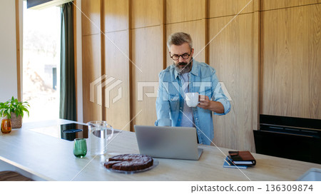 Man working from home office, drinking coffe and working on laptop. Man working from home office, drinking coffe and working on laptop. 136309874