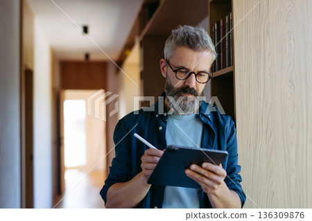 Man standing by the window with tablet and writing notes. Man standing by the window with tablet and writing notes. 136309876