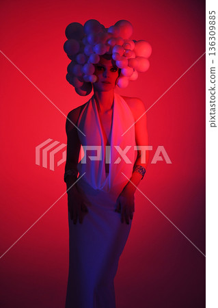Avant-garde fashion woman wearing sculptural headpiece and white gown 136309885