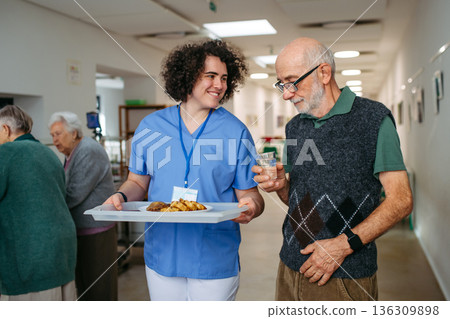 Senior man having lunch with supportive caregiver in community center cafeteria. Senior man having lunch with supportive caregiver in community center cafeteria. 136309898