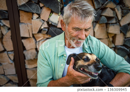 Older man with dog in front of wooden logs. Older man with dog in front of wooden logs. 136309945