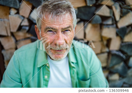 Older man with gray hair posing in front of wooden logs. Older man with gray hair posing in front of wooden logs. 136309946