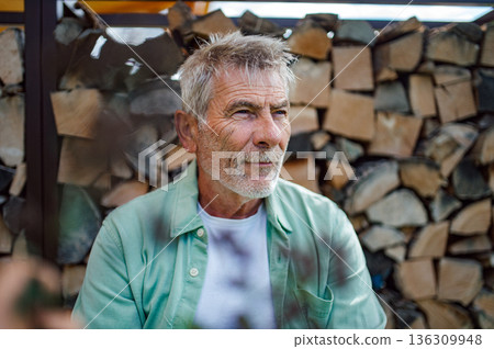 Portrait of senior man standing outdoors near stacked firewood. Portrait of senior man standing outdoors near stacked firewood. 136309948