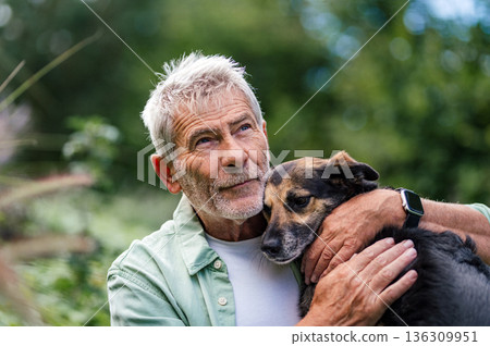 Senior man embracing loyal dog, relaxing outdoor moment Senior man embracing loyal dog, relaxing outdoor moment 136309951
