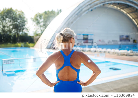 Older female swimmer getting ready for regular fitness swimming. Older female swimmer getting ready for regular fitness swimming. 136309954