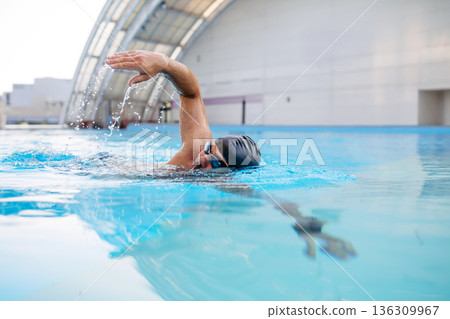 Focused swimmer performing crawl stroke in water. 136309967