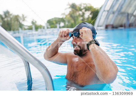 Male swimmer is preparing for swim in pool. 136309969