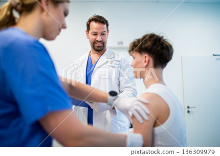 Doctor giving flu vaccine to teenage boy in medical clinic. 136309979
