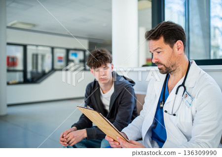 Doctor talking with teenage patient in hospital waiting room. 136309990