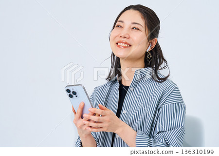 一位戴著耳機、手持智慧型手機的年輕女子 136310199