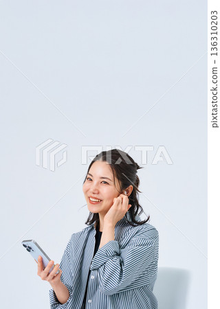 一位戴著耳機、手持智慧型手機的年輕女子 136310203