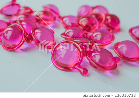 Close-up macro shot of many glossy pink hair treatment capsules. Focused foreground highlights the rich oil and reflective texture Close-up macro shot of many glossy pink hair treatment capsules. Focused foreground highlights the rich oil and reflective texture 136310738