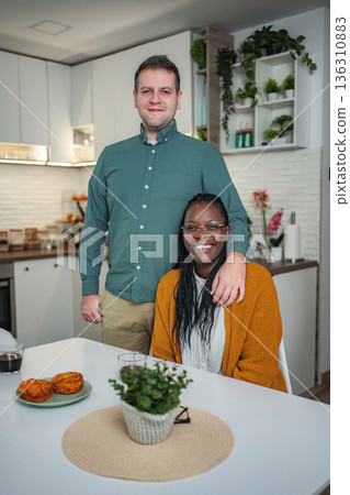 Interracial couple posing in kitchen, embracing, smiling at camera Interracial couple posing in kitchen, embracing, smiling at camera 136310883