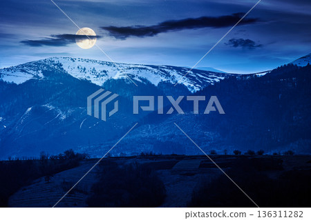 carpathian mountains of ukraine in early spring at night. view of countryside landscape with rolling hills and snow covered peak in full moon light. inner strength to overcome fear and loneliness 136311282