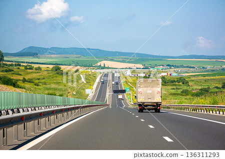 cars on Romania highway. asphalt road to mountain. vast summer landscape in dappled light. transportation background of europe. picturesque motorway wallpaper on a sunny day cars on Romania highway. asphalt road to mountain. vast summer landscape in dappled light. transportation background of europe. picturesque motorway wallpaper on a sunny day 136311293