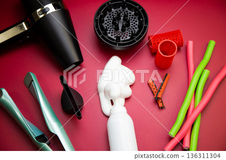 Top view on a pink background, a hairdryer with attachments, stylers and curling irons for straightening and creating curls, foam for creating volume and long-term holding, curlers of different shapes Top view on a pink background, a hairdryer with attachments, stylers and curling irons for straightening and creating curls, foam for creating volume and long-term holding, curlers of different shapes 136311304