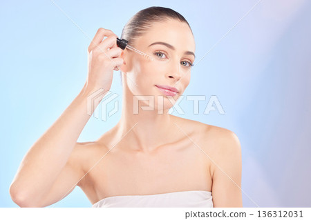 Woman, portrait and serum for face in studio, aesthetic skincare or dermatology on blue background. Female model, facial cosmetics and dropper of hyaluronic acid, collagen and oil product for beauty 136312031