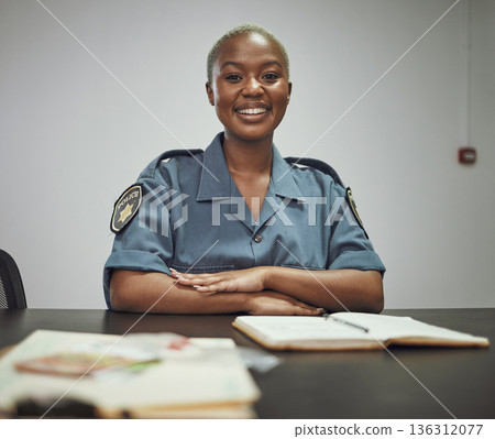 Happy, smile and portrait of a female police officer sitting by a desk in the office writing reports. Confidence, happiness and African woman security guard with a positive mindset in the workplace. 136312077