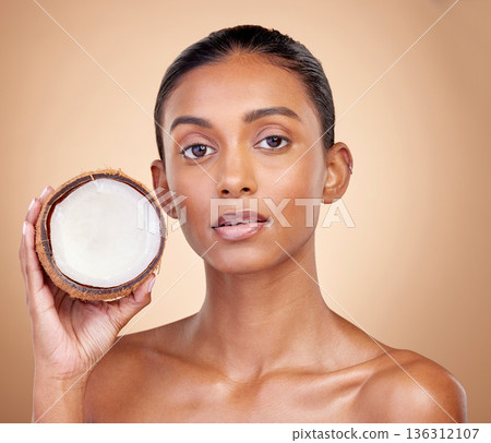 Woman face, coconut fruit and beauty, healthy skincare or vegan cream on brown studio background. Portrait of Indian person in natural product for dermatology, eco friendly cosmetics and oil benefits Woman face, coconut fruit and beauty, healthy skincare or vegan cream on brown studio background. Portrait of Indian person in natural product for dermatology, eco friendly cosmetics and oil benefits 136312107