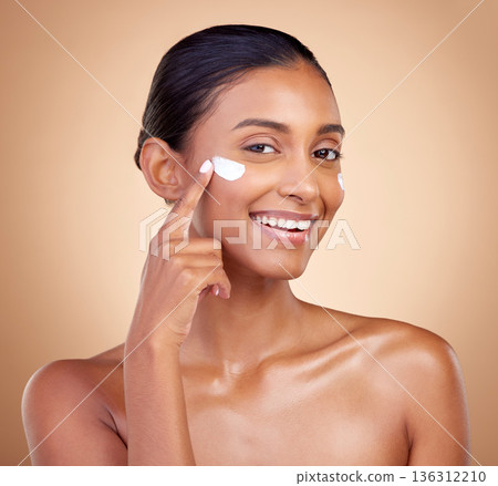 Face, cream and portrait of happy indian woman, makeup cosmetics and skincare dermatology on studio background. Young female model, lotion and facial sunscreen for clean beauty, shine and self care Face, cream and portrait of happy indian woman, makeup cosmetics and skincare dermatology on studio background. Young female model, lotion and facial sunscreen for clean beauty, shine and self care 136312210