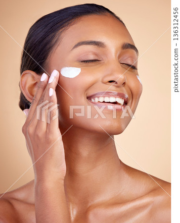 Woman, happy skincare and cream for facial beauty, apply lotion and dermatology or cosmetics. Skin care product, face and young person or model sunscreen or moisturizer on a brown studio background 136312456