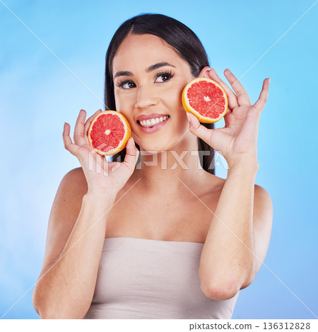 Woman thinking, happy skincare and grapefruit for beauty, cosmetics, natural product and tropical facial or vitamin c. Young person or model with red fruits for dermatology on blue, studio background Woman thinking, happy skincare and grapefruit for beauty, cosmetics, natural product and tropical facial or vitamin c. Young person or model with red fruits for dermatology on blue, studio background 136312828