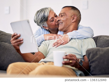 Senior couple, hug and tablet on sofa to relax with quality time in home with kiss during retirement. Couple, technology and embrace with elderly man or woman in living room together on couch. Senior couple, hug and tablet on sofa to relax with quality time in home with kiss during retirement. Couple, technology and embrace with elderly man or woman in living room together on couch. 136312840