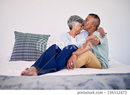 Love, kiss and senior couple on their bed in their home while relaxing, bonding and spending time together. Happy, affection and elderly man and woman in retirement resting in bedroom in their house. 136312873
