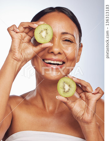 Face, skincare and senior woman with kiwi in studio isolated on a white background. Food, natural fruit and portrait of happy model with nutrition for wellness, healthy diet and anti aging for beauty 136313183