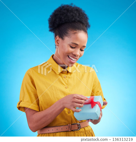 Happy, gift and a black woman in studio with a surprise for birthday, celebration or holiday. Fashion, present and african female person on a blue background with a box, ribbon and prize or package Happy, gift and a black woman in studio with a surprise for birthday, celebration or holiday. Fashion, present and african female person on a blue background with a box, ribbon and prize or package 136313219