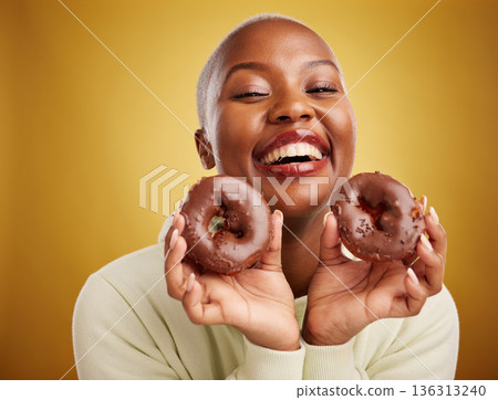 Portrait, food and donut with a black woman in studio on a gold background for candy or unhealthy eating. Smile, chocolate and baking with a happy young female person holding sweet pastry for dessert Portrait, food and donut with a black woman in studio on a gold background for candy or unhealthy eating. Smile, chocolate and baking with a happy young female person holding sweet pastry for dessert 136313240