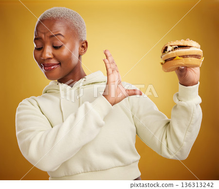 Diet, reject and fast food with woman or nutrition in yellow background is unhappy. Burger, no and girl is frustrated with choice in studio with mistake or refuse with meal for weight or health. Diet, reject and fast food with woman or nutrition in yellow background is unhappy. Burger, no and girl is frustrated with choice in studio with mistake or refuse with meal for weight or health. 136313242