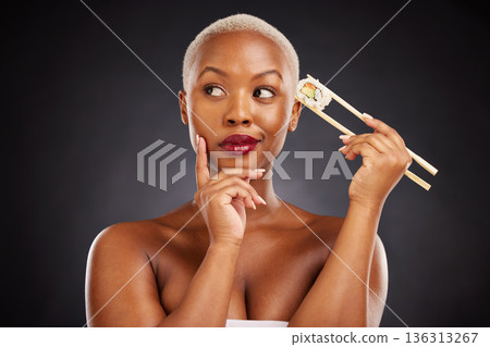 Thinking, idea and woman with sushi and chopsticks in studio for healthy eating, beauty or food. Black female model with makeup on dark background for wellness glow, diet or seafood advertising Thinking, idea and woman with sushi and chopsticks in studio for healthy eating, beauty or food. Black female model with makeup on dark background for wellness glow, diet or seafood advertising 136313267