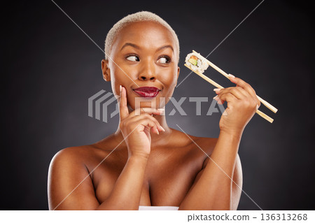 Sushi, thinking and face of a woman with chopsticks in studio for healthy eating, beauty or food. Black female model with makeup on dark background for wellness glow, diet or seafood advertising idea Sushi, thinking and face of a woman with chopsticks in studio for healthy eating, beauty or food. Black female model with makeup on dark background for wellness glow, diet or seafood advertising idea 136313268