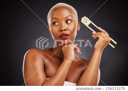 Face, thinking and woman with sushi and chopsticks in studio for healthy eating, beauty or food. Black female model with makeup idea on dark background for wellness glow, diet or seafood advertising Face, thinking and woman with sushi and chopsticks in studio for healthy eating, beauty or food. Black female model with makeup idea on dark background for wellness glow, diet or seafood advertising 136313270