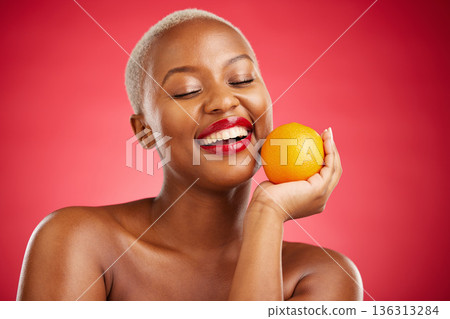 Orange, smile and black woman with natural beauty, dermatology and vitamin c on a red studio background. Female person, happy or model with citrus fruit, health or wellness with cosmetics or skincare 136313284