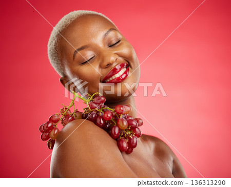 Skincare, smile and grapes with a model black woman in studio on a red background for health or nutrition. Beauty, happy and fruit with a young female person posing for wellness, diet or detox 136313290