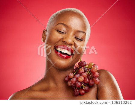 Beauty, smile and grapes with a model black woman in studio on a red background for health or nutrition. Skincare, happy and fruit with a young female person posing for wellness, diet or detox 136313292