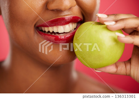 Woman, mouth and apple for natural nutrition, diet or health and wellness against a red studio background. Closeup of female person smile with lipstick and organic fruit for vitamin, fiber or food 136313301