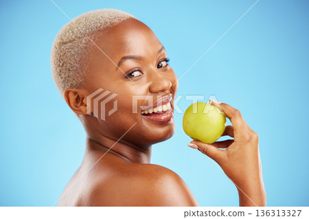 Happy black woman, portrait and apple for diet, nutrition or health and wellness against a blue studio background. Face of African female person with natural organic fruit for vitamin, fiber or food Happy black woman, portrait and apple for diet, nutrition or health and wellness against a blue studio background. Face of African female person with natural organic fruit for vitamin, fiber or food 136313327