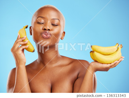 Black woman, banana and diet for potassium, vitamin or fiber against a blue studio background. Face of calm African female person with bunch of yellow fruit for health and wellness on mockup space 136313343