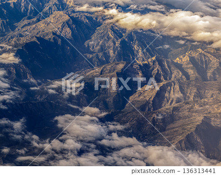 Aerial View Of Rugged Mountain Range With Clouds Casting Golden Light Over Craggy Summits At Dusk 136313441