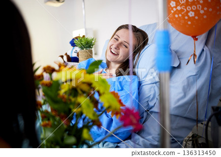 Hospital, sick patient and visitor with flowers at bed with a woman in recovery with support. Healthcare, medical insurance and person with bouquet, family and care with get well soon balloons Hospital, sick patient and visitor with flowers at bed with a woman in recovery with support. Healthcare, medical insurance and person with bouquet, family and care with get well soon balloons 136313450